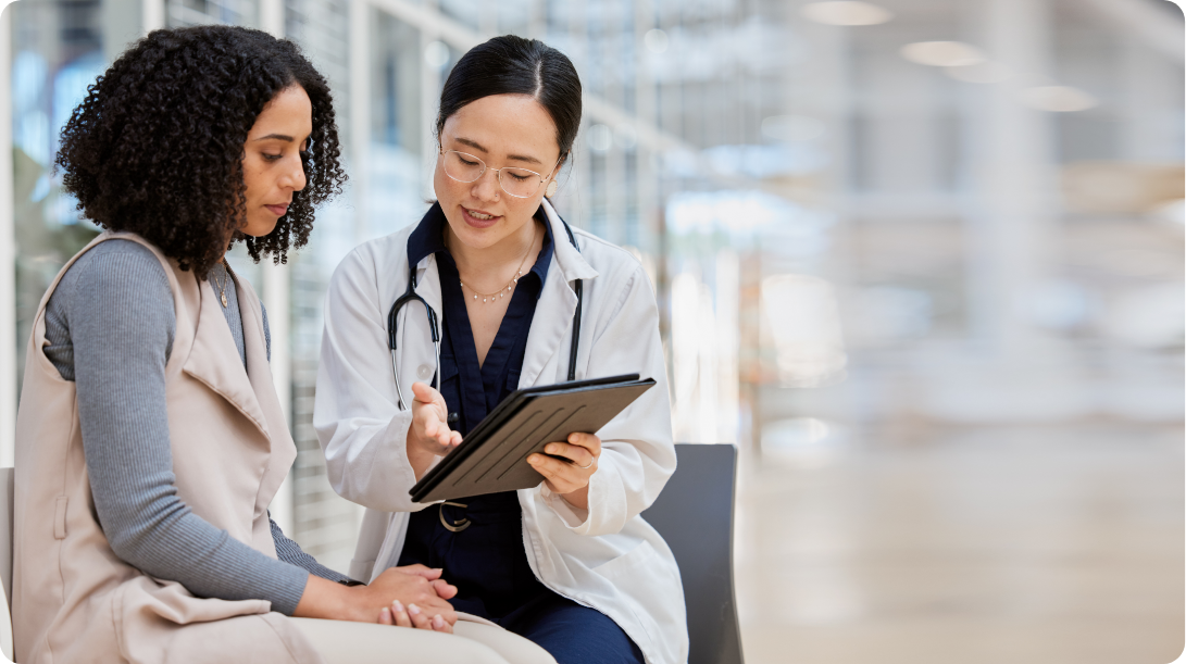 A doctor and patient sitting together, focused on a digital tablet while discussing safety considerations and patient monitoring.